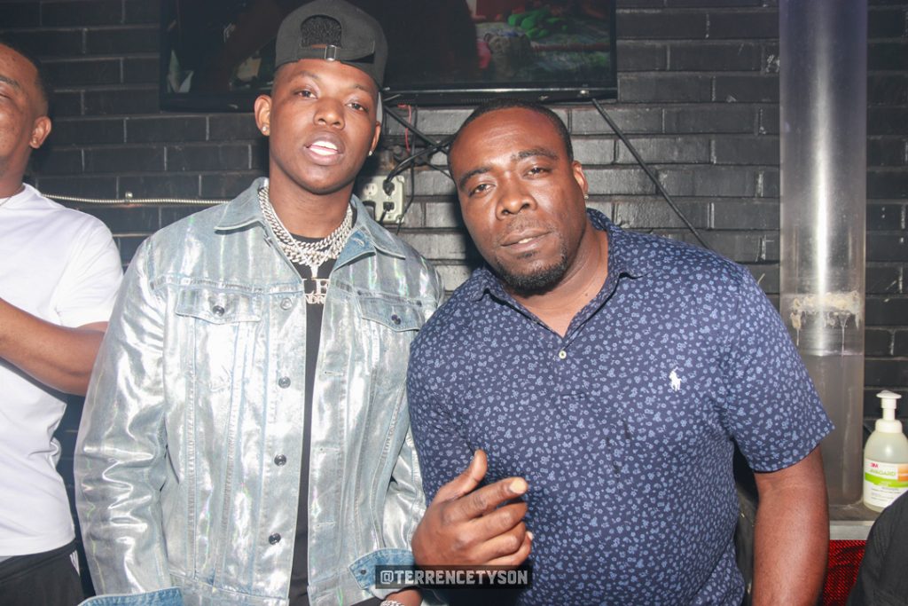 Rapper Yung Bleu wearing silver jacket ständig next to man in blue shirt